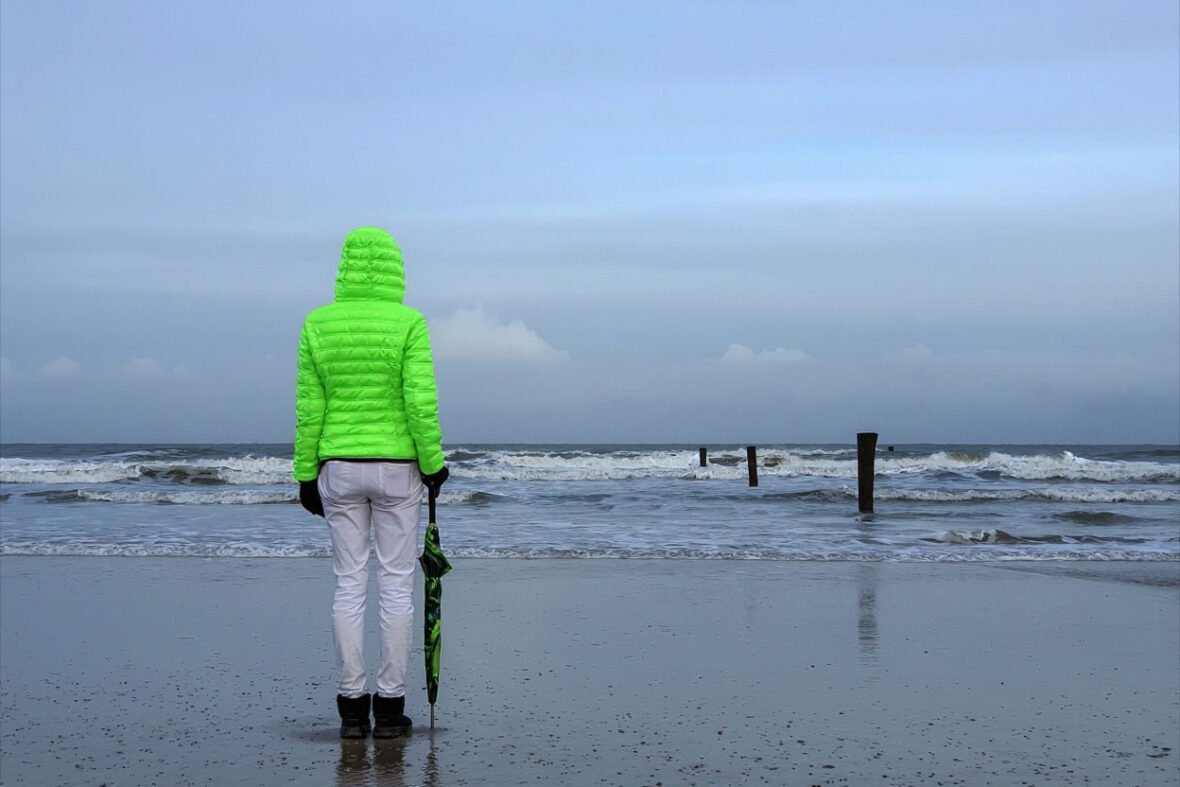 Mensch in grüner Jacke steht am Strand
