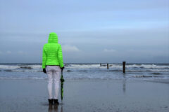 Mensch in grüner Jacke steht am Strand